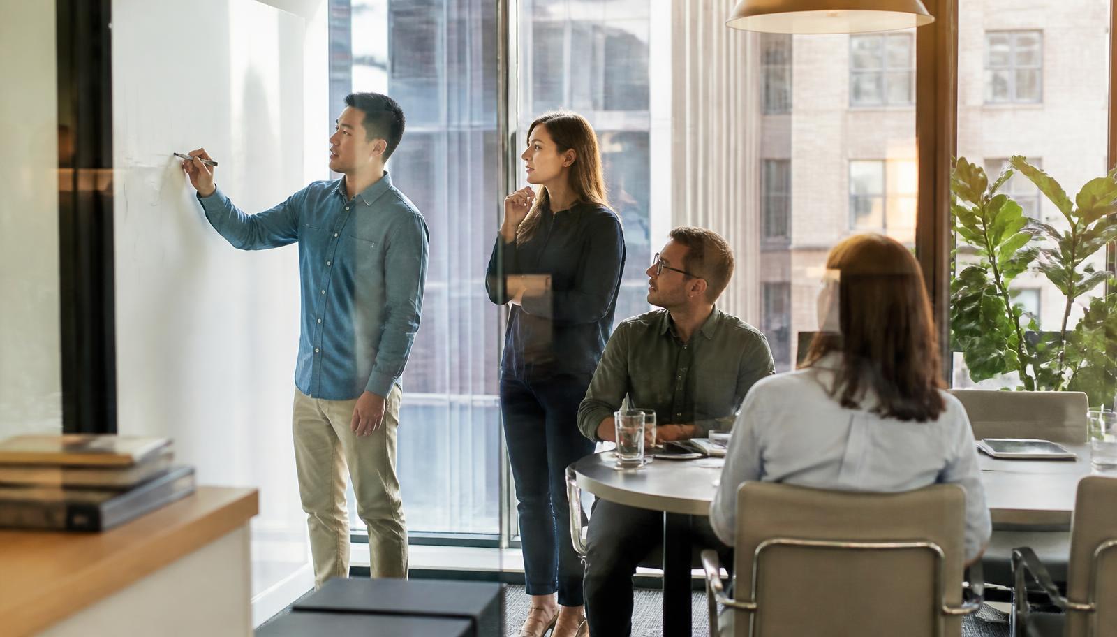Team collaborating around a whiteboard in a glass-walled meeting room